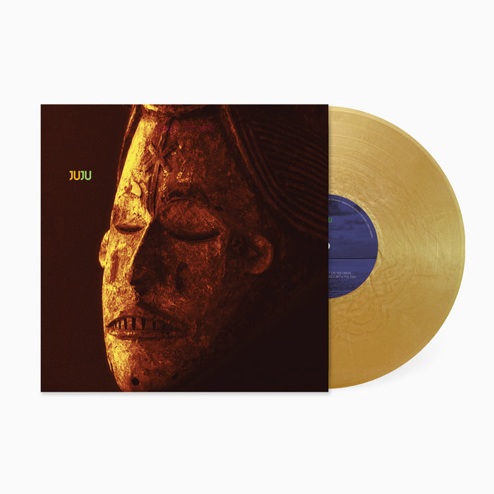A 180g gold nugget vinyl record partially slides out from an album cover featuring a close-up of an African mask, titled "Juju - Juju" in yellow text—a striking homage to the debut album’s psychedelic roots.